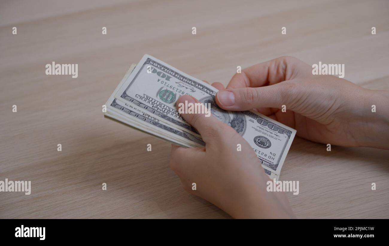 Women's hands hold hundred dollar bills and methodically count them