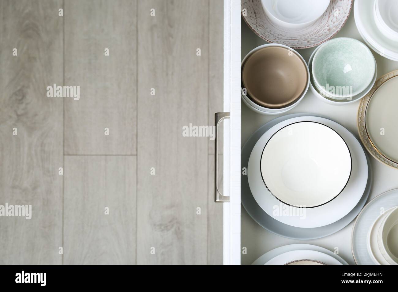 Open drawer with different plates and bowls in kitchen, top view. Space