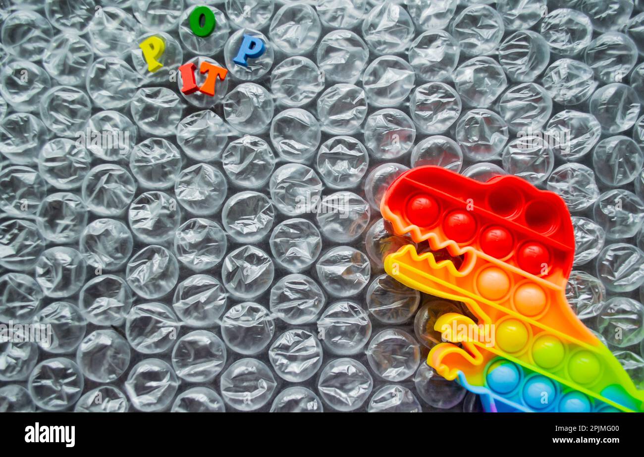Toy pop it dinosaur rainbow colors on a bubble wrap background with multicolored letters - Pop it. Copy space. Stock Photo