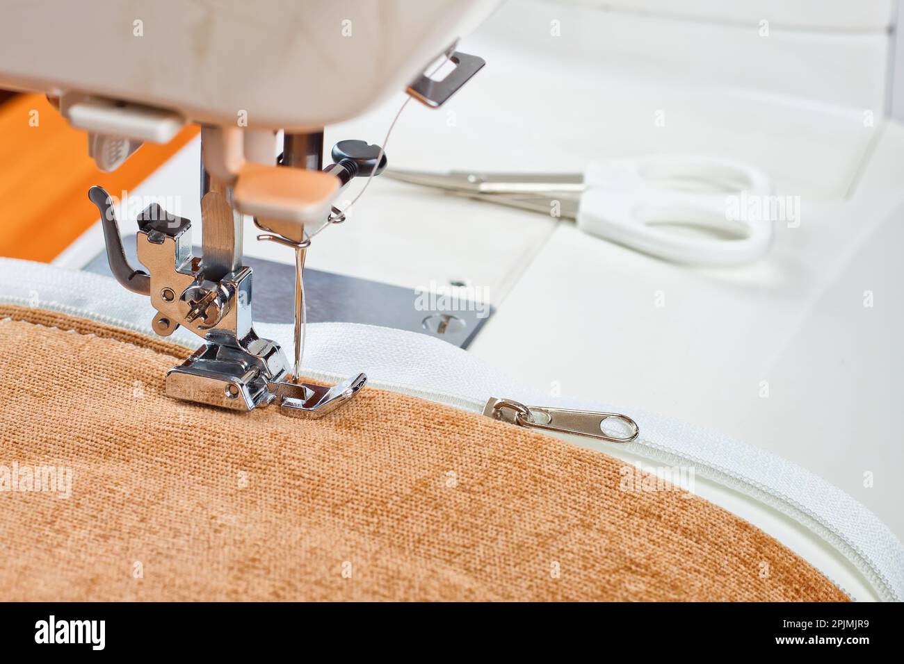 Modern sewing machine sews on the zipper on beige item of clothing