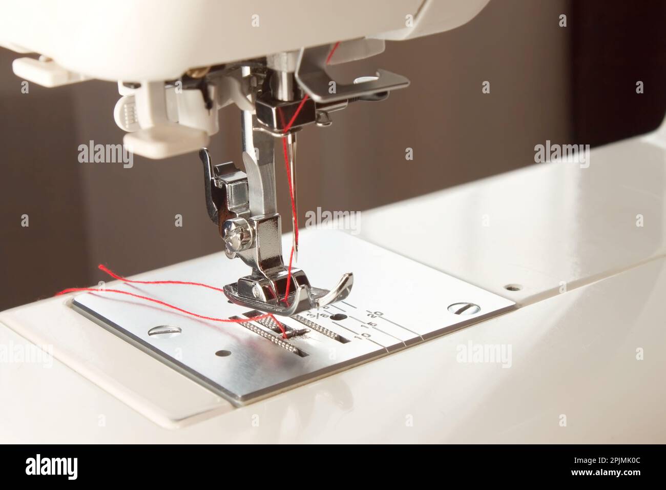 white modern sewing machine presser foot and needle with red thread