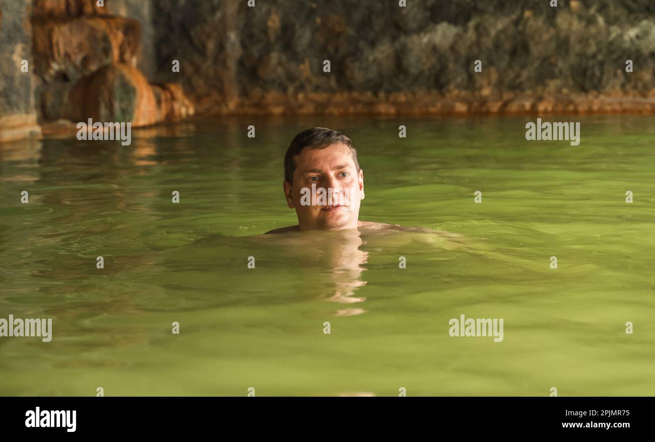 Man bathe swim in outdoor cave, dirty hot springs. Thermal water bath