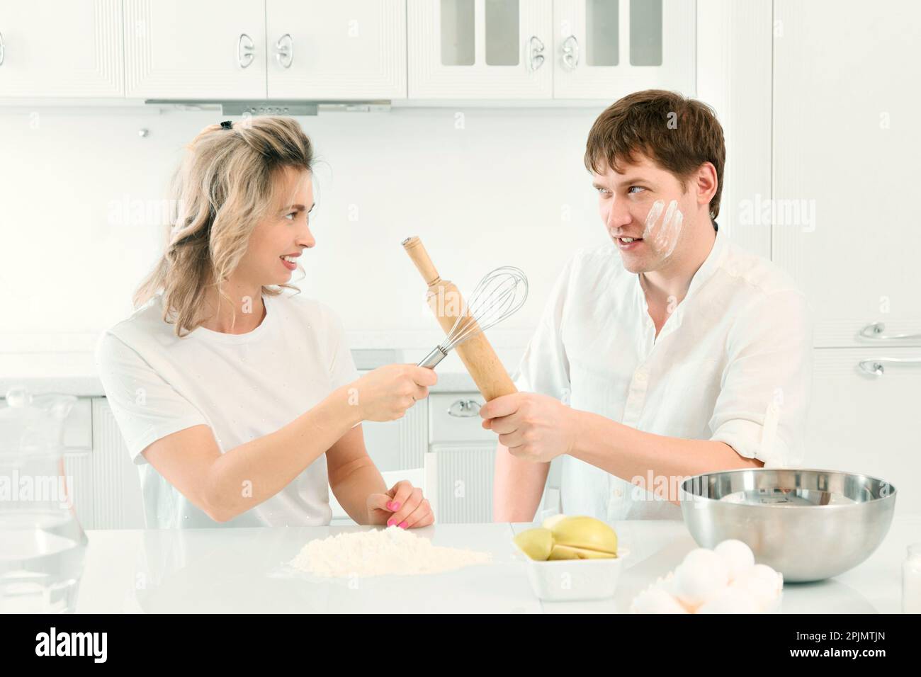 Husband and wife quarrel in kitchen while cooking. Comic and cheerful confrontation between man and woman in kitchen. Background.. Stock Photo
