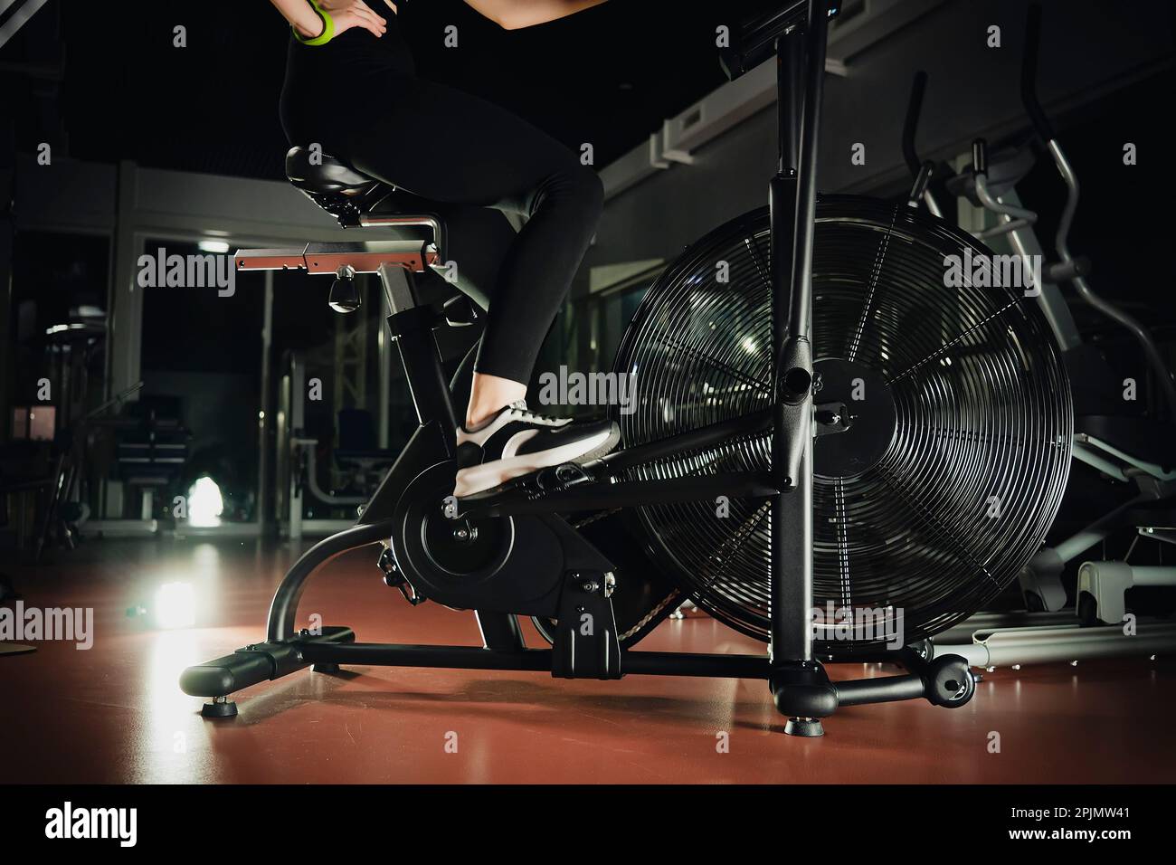 Closeup of spinning wheel on exercise bike on spin bicycle fitness workout. Woman training on stationary bike watching online video class for exercisi Stock Photo