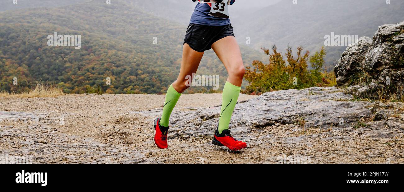 legs female runner in compression socks run mountain trail marathon, jogging in cloudy autumn weather through mountainous terrain Stock Photo