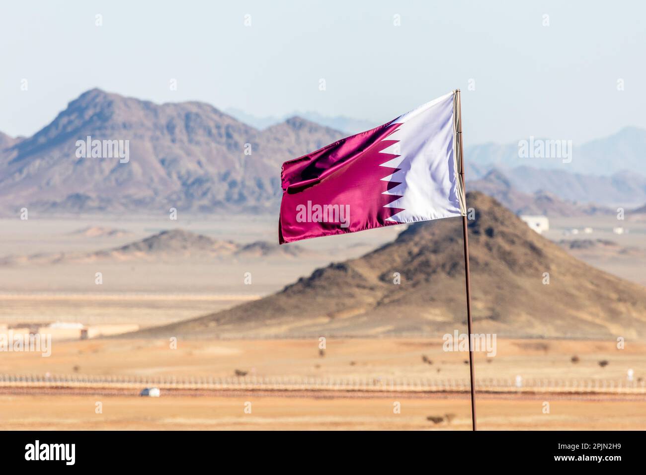 Qatar flag waving on the wind in Saudi Arabian desertwith mountains in