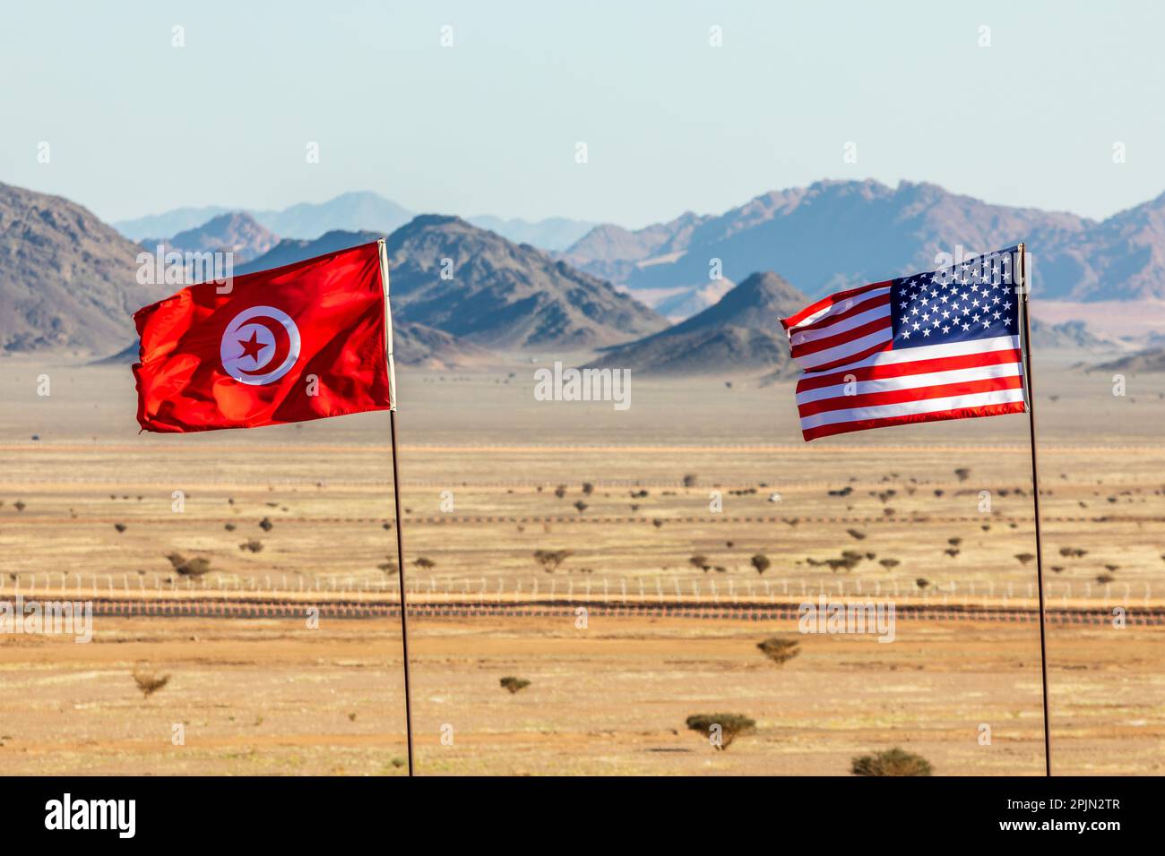 US and Tunisian flags waving togetner on the wind in Saudi Arabian desertwith mountains in background, Al Ula, Saudi Arabia Stock Photo