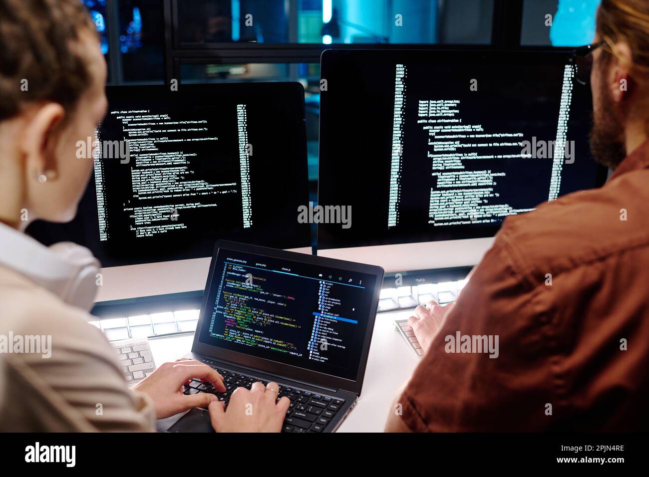Close-up of two young developers working over data decoding software while young female IT engineer typing on laptop keyboard Stock Photo