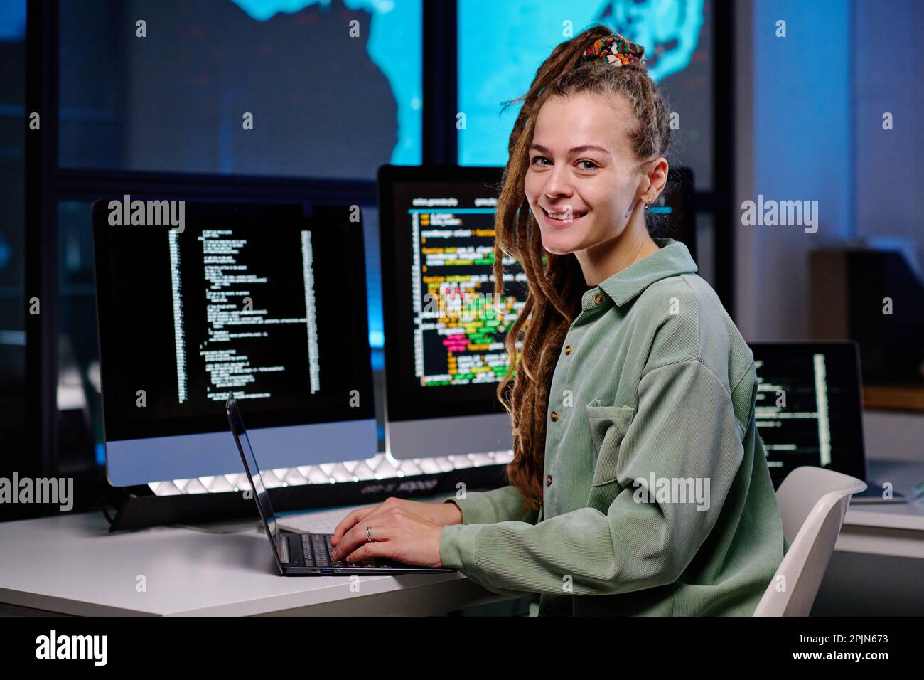 Young successful female programmer looking at camera by workplace with group of desktop computers with coded data on their screens Stock Photo