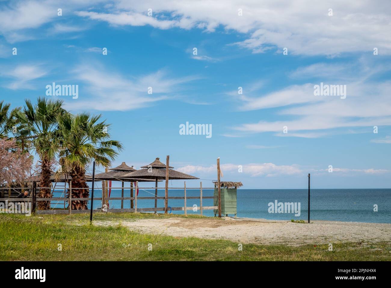 Summer seascape scenery with palm trees and straw umbrellas at a beach of Aegean sea Stock Photo