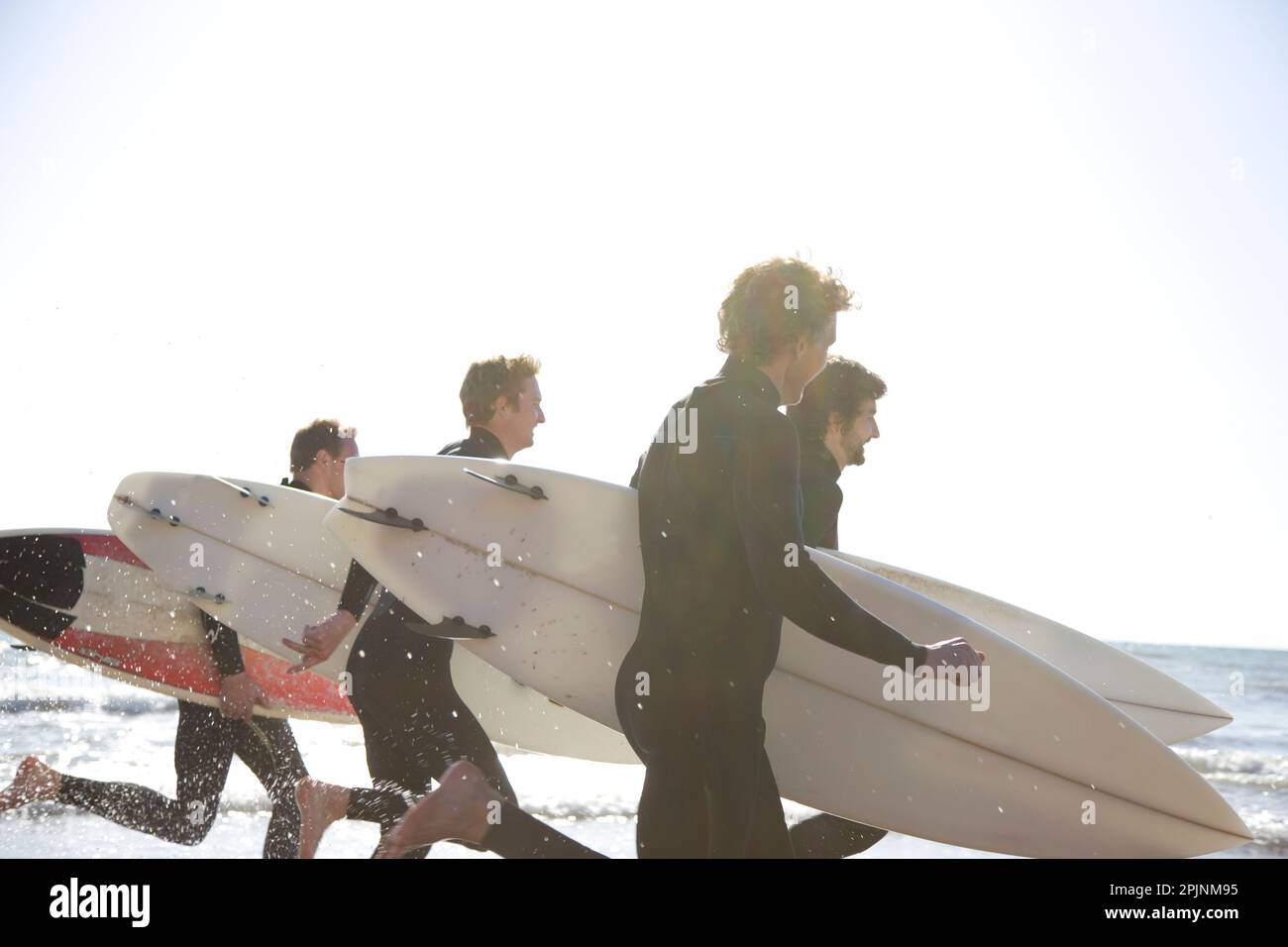 Surfers running on the beach holding surfboards Stock Photo Alamy