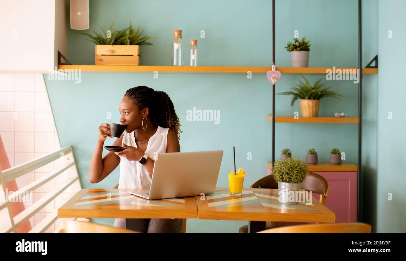 Pretty young black woman drinking coffee while working on laptop in the ...