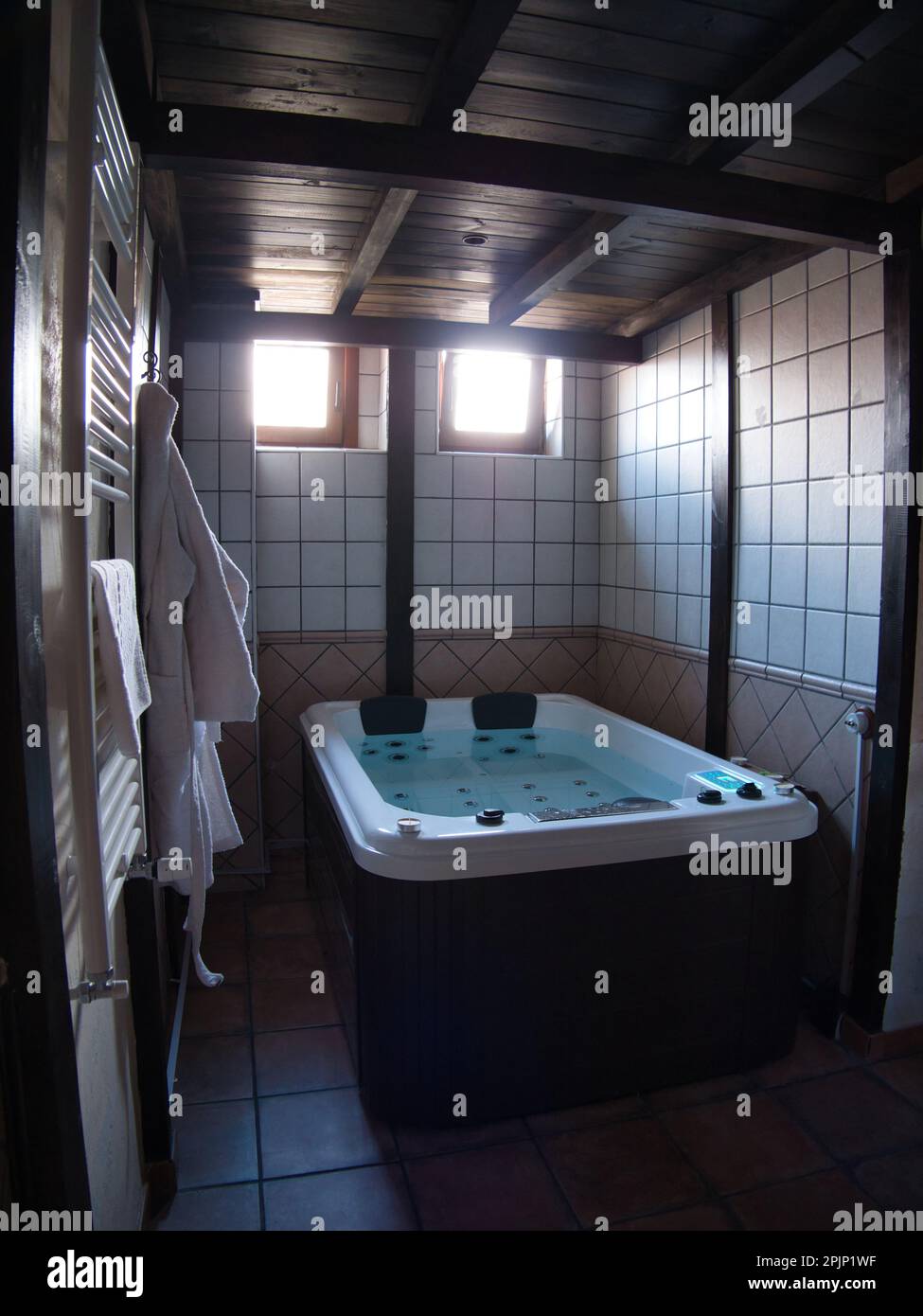 A bathroom features a hot tub, with white towels and bathrobes hanging on the wall Stock Photo