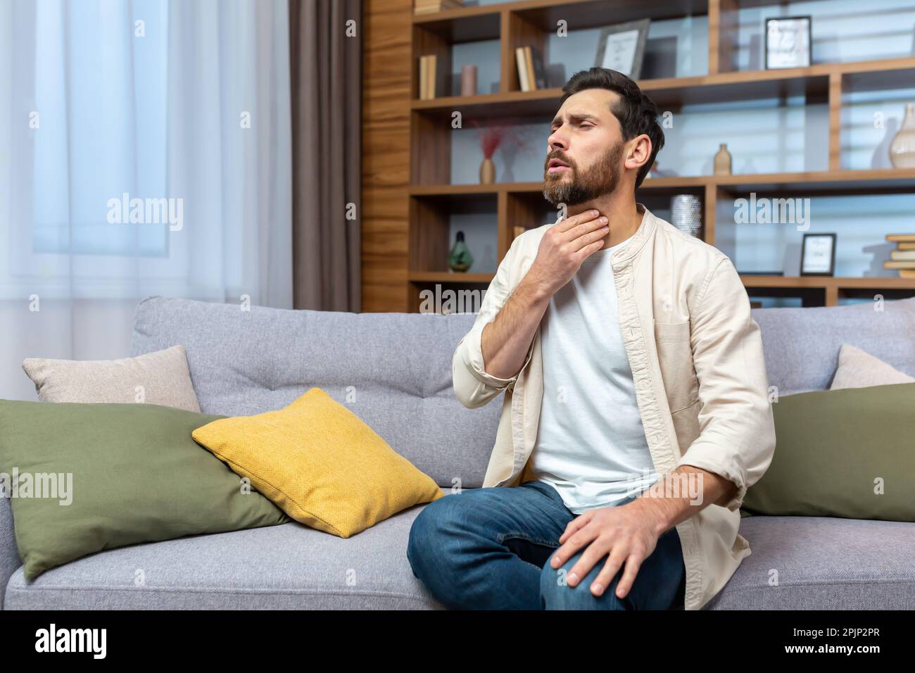 Sore throat. A young man sits at home on the sofa and holds his throat