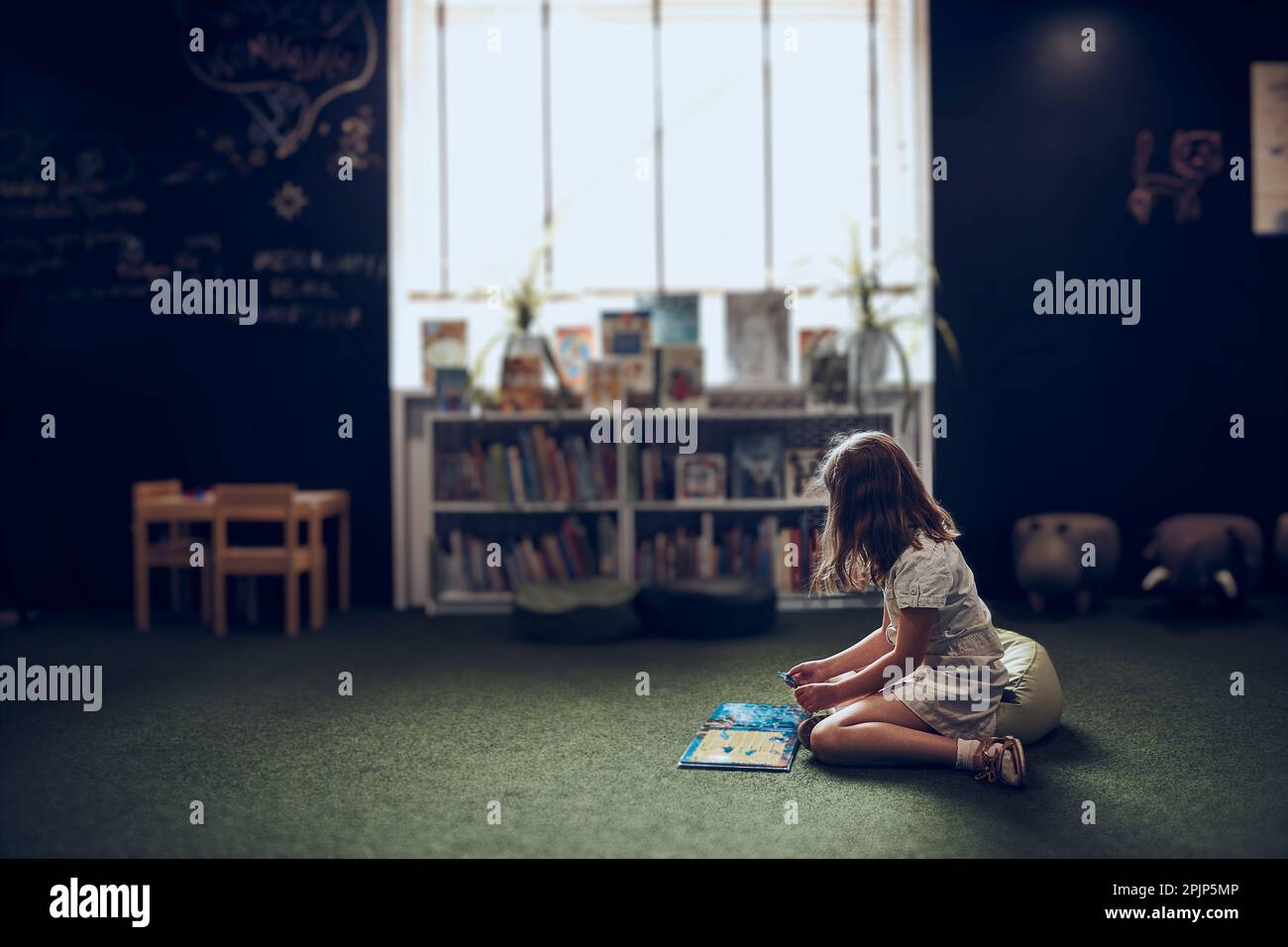 Child solving riddle in book in school library. Primary school pupil is involved in book with riddles. Smart girl learning to solve problems. Benefits Stock Photo