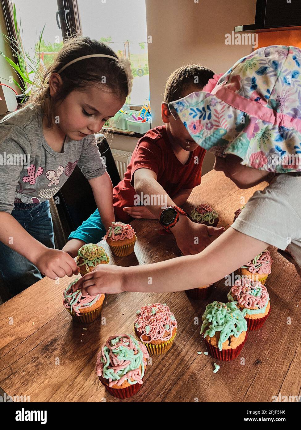 Group of children baking cupcakes, preparing ingredients, topping, sprinkles for decorating cookies. Kids cooking, working together in kitchen at home Stock Photo