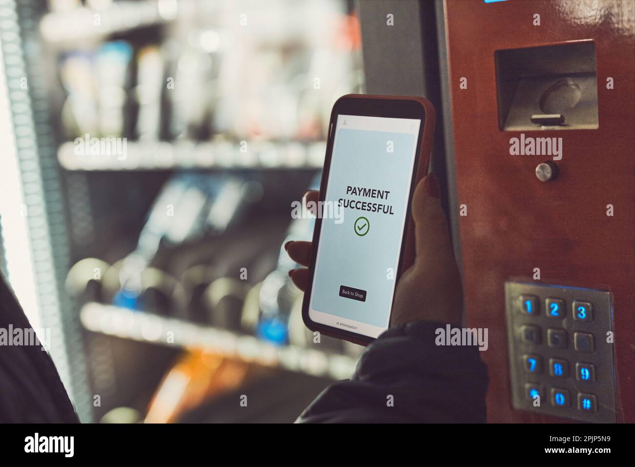 Consumer paying for product at vending machine using contactless method of payment with mobile phone. Woman using payment app on smartphone to buy pro Stock Photo