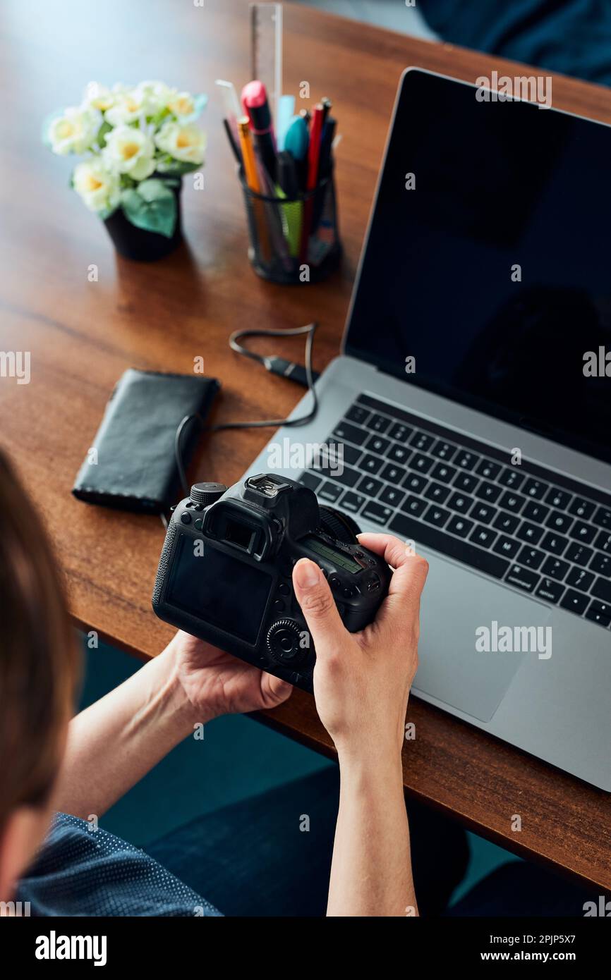 Female photographer working on photos on laptop and camera. Woman editing retouching browsing photos working as a freelancer sitting at desk Stock Photo