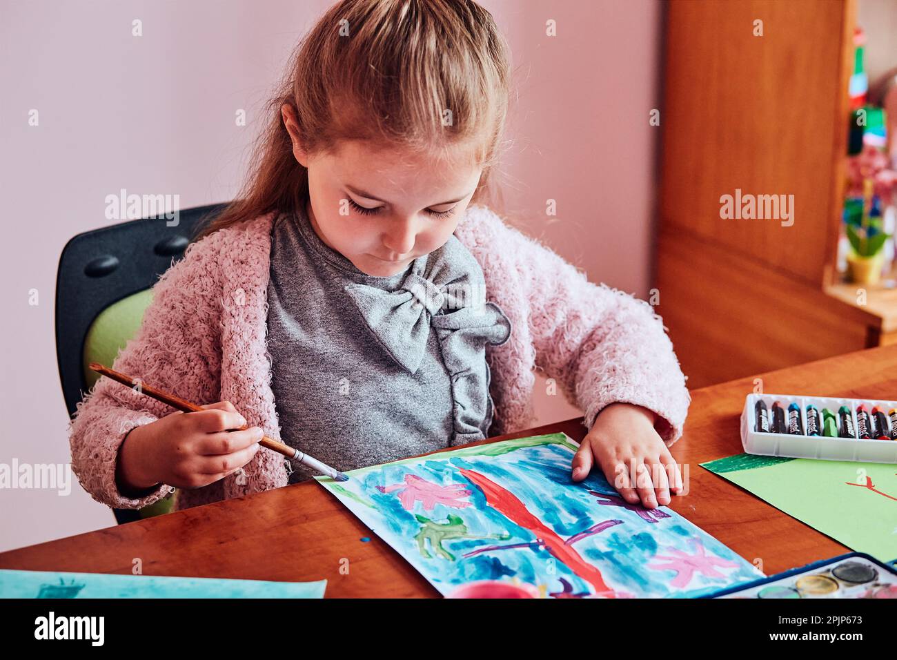 Little girl preschooler painting a picture using colorful paints and crayons. Child having fun making a picture during an art class in the classroom Stock Photo