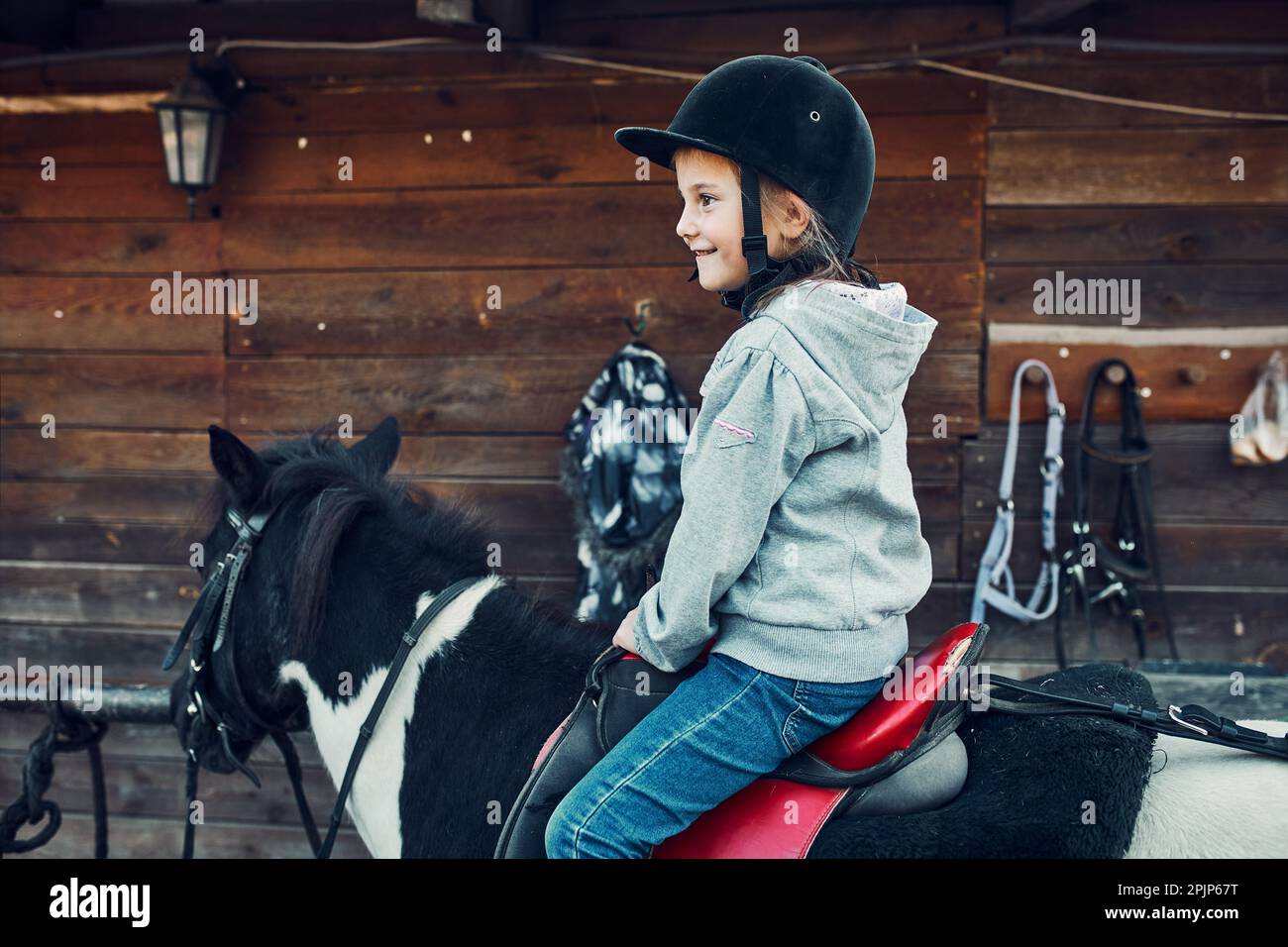 Little smiling girl learning horseback riding. 5-6 years old equestrian in helmet having fun riding a horse Stock Photo