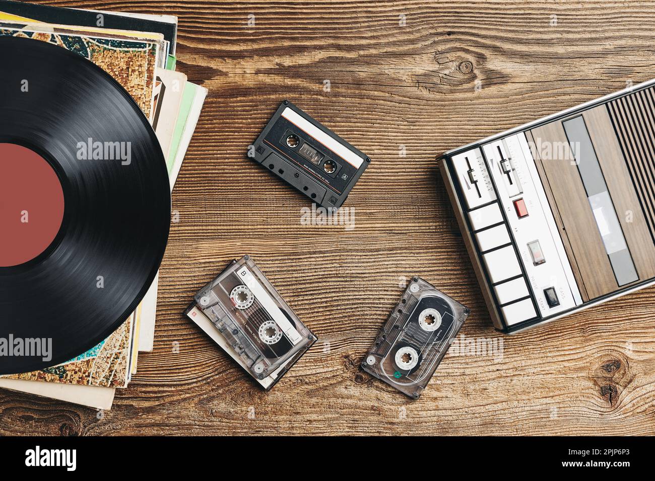 Vinyl records, cassette tapes and cassette recorder on wooden table. Retro music style. 80s music party. Vintage style. Analog equipment. Stereo sound Stock Photo