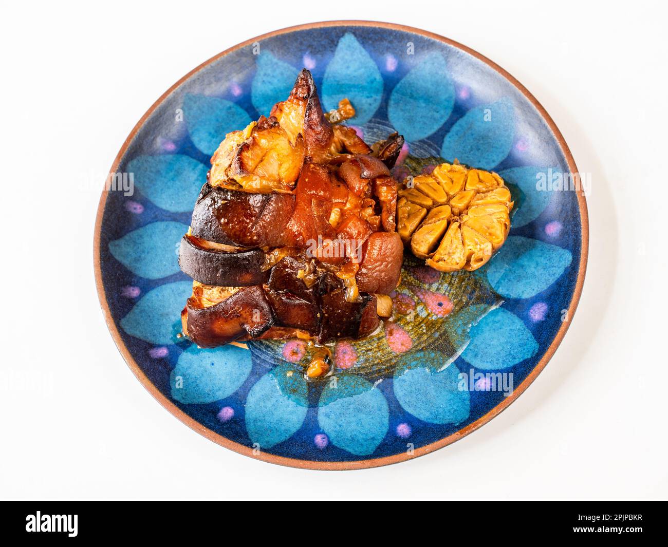 Baked pork belly and garlic on decorative blue plate on white background, closeup. Stock Photo