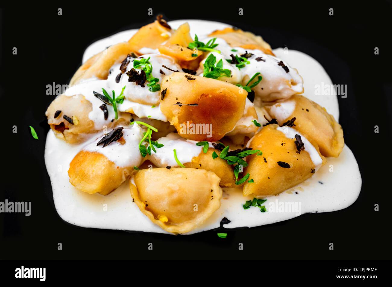 Roasted stuffed dumpling with creamy sauce, pea shoot on black plate, closeup. Stock Photo