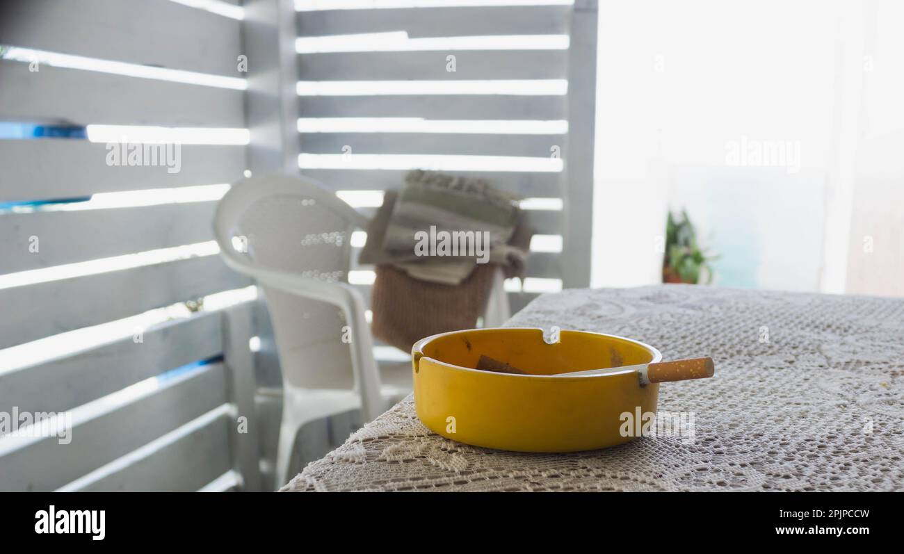 A high-resolution, close-up image of a yellow ashtray with a single cigarette placed in the center Stock Photo