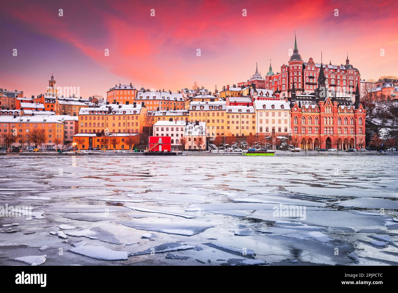 Stockholm, Sweden. Mariaberget and Sodermalm island in winter. Beautiful orange, violet and pink sky at sunset, reflected in frozen water of lake Mala Stock Photo