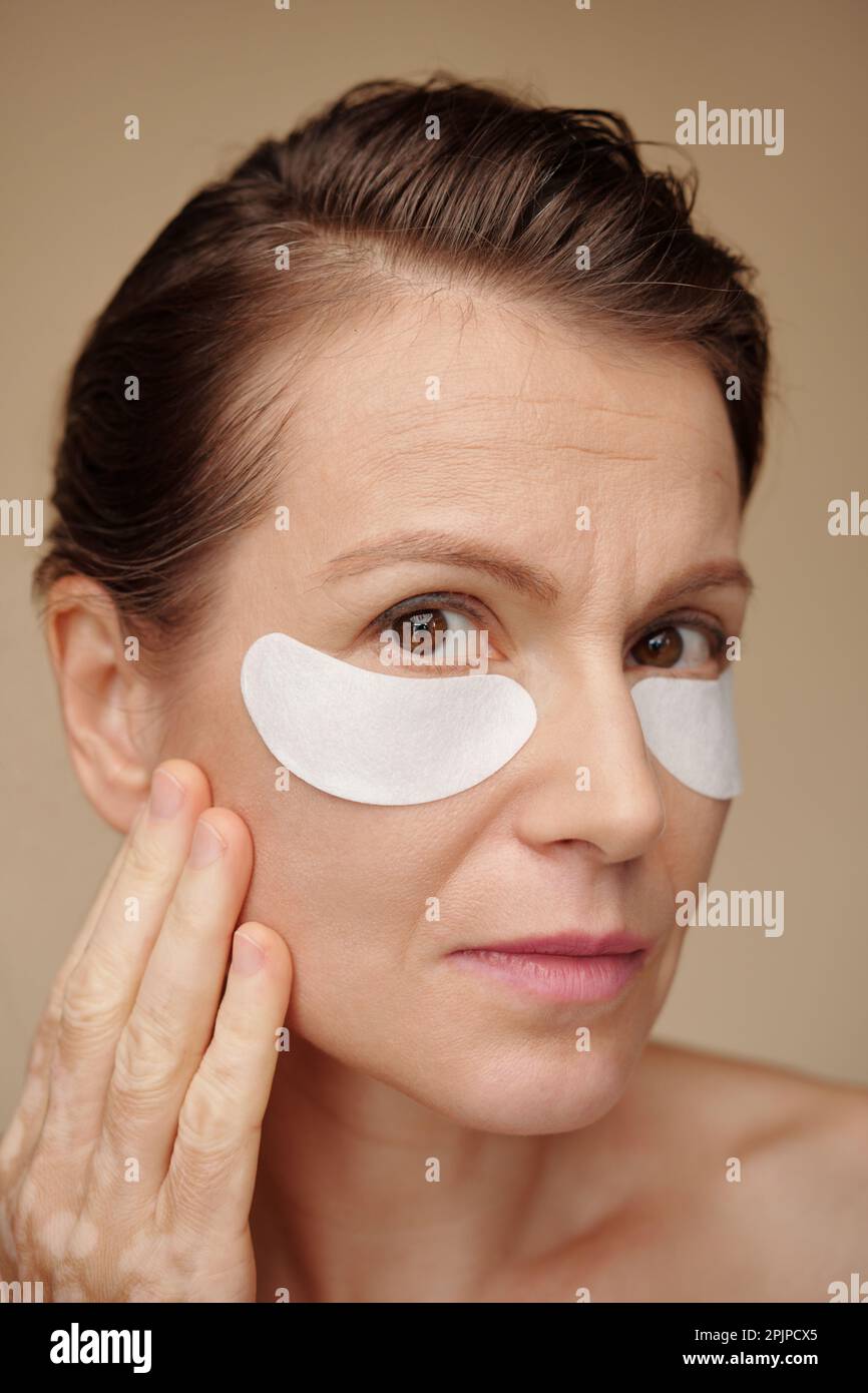 Portrait of middleaged woman applying patches under eyes to get rid of