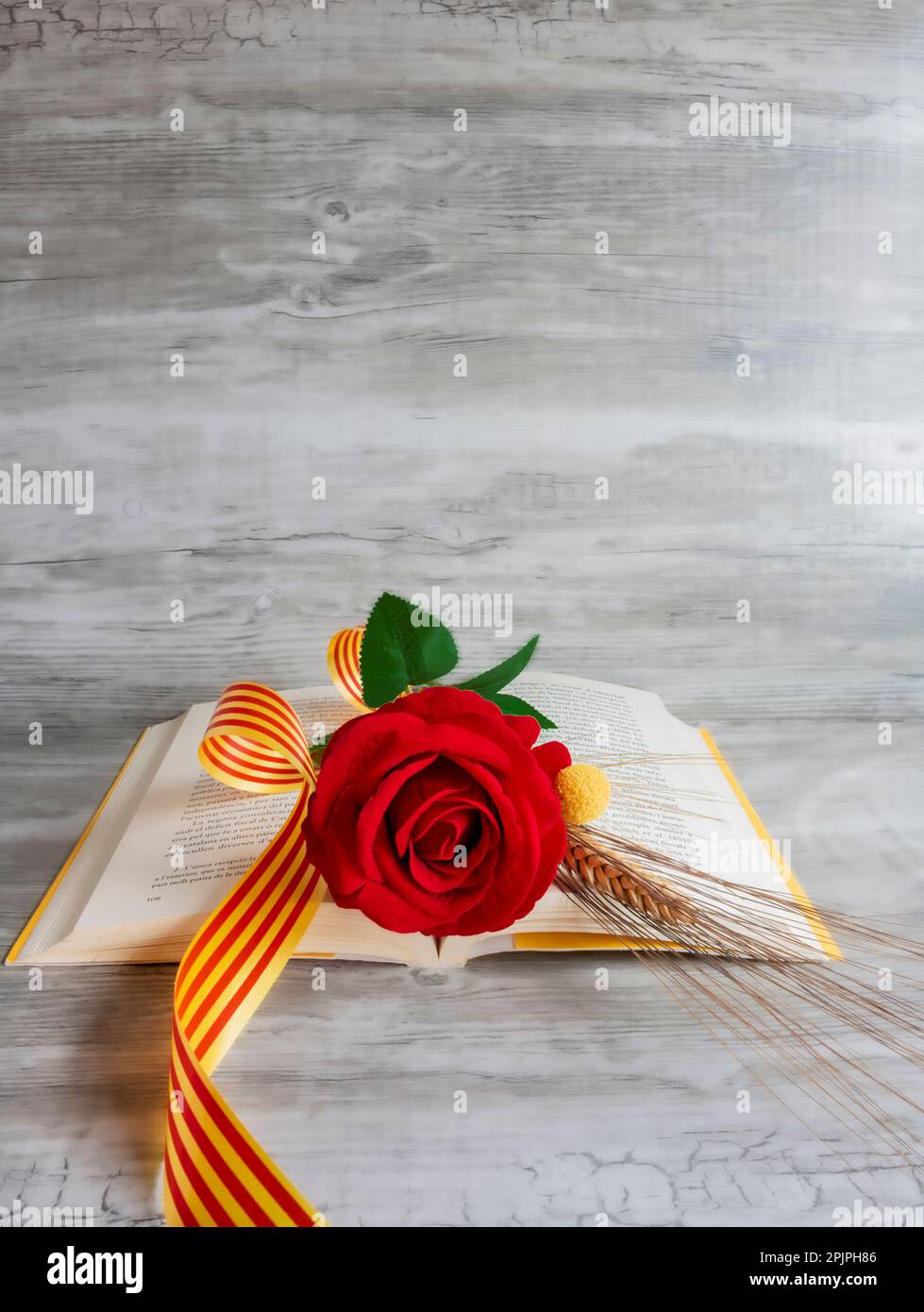 Rose and yellow book, ear of wheat, with Catalan flag and red ribbon, on beige background with texture, vertical, copy space, valentine’s day Stock Photo