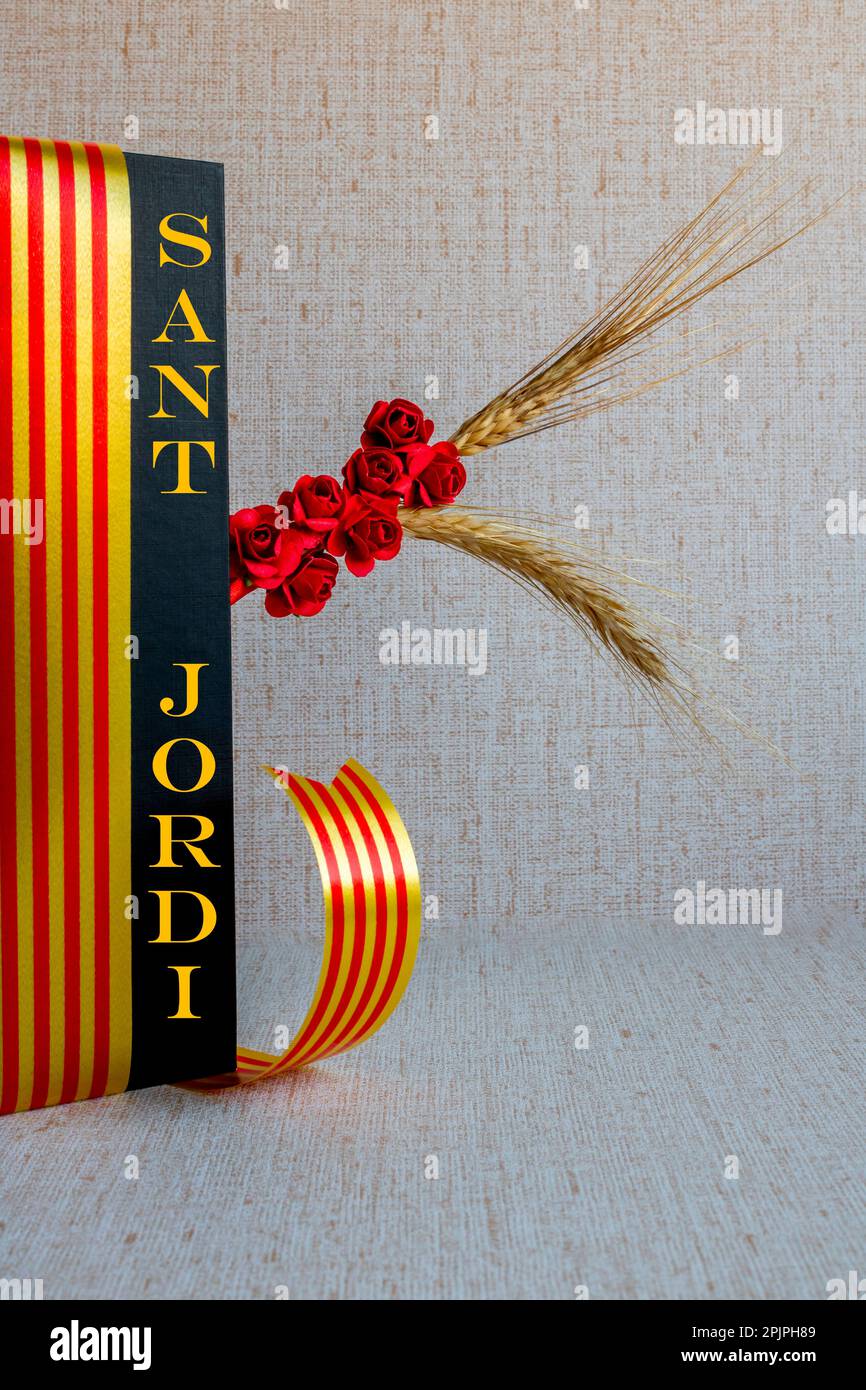 Sant Jordi, ceramic figure on a book with black covers, a red paper rose, book behind with a blank sheet with a ribbon of the Catalan flag Stock Photo