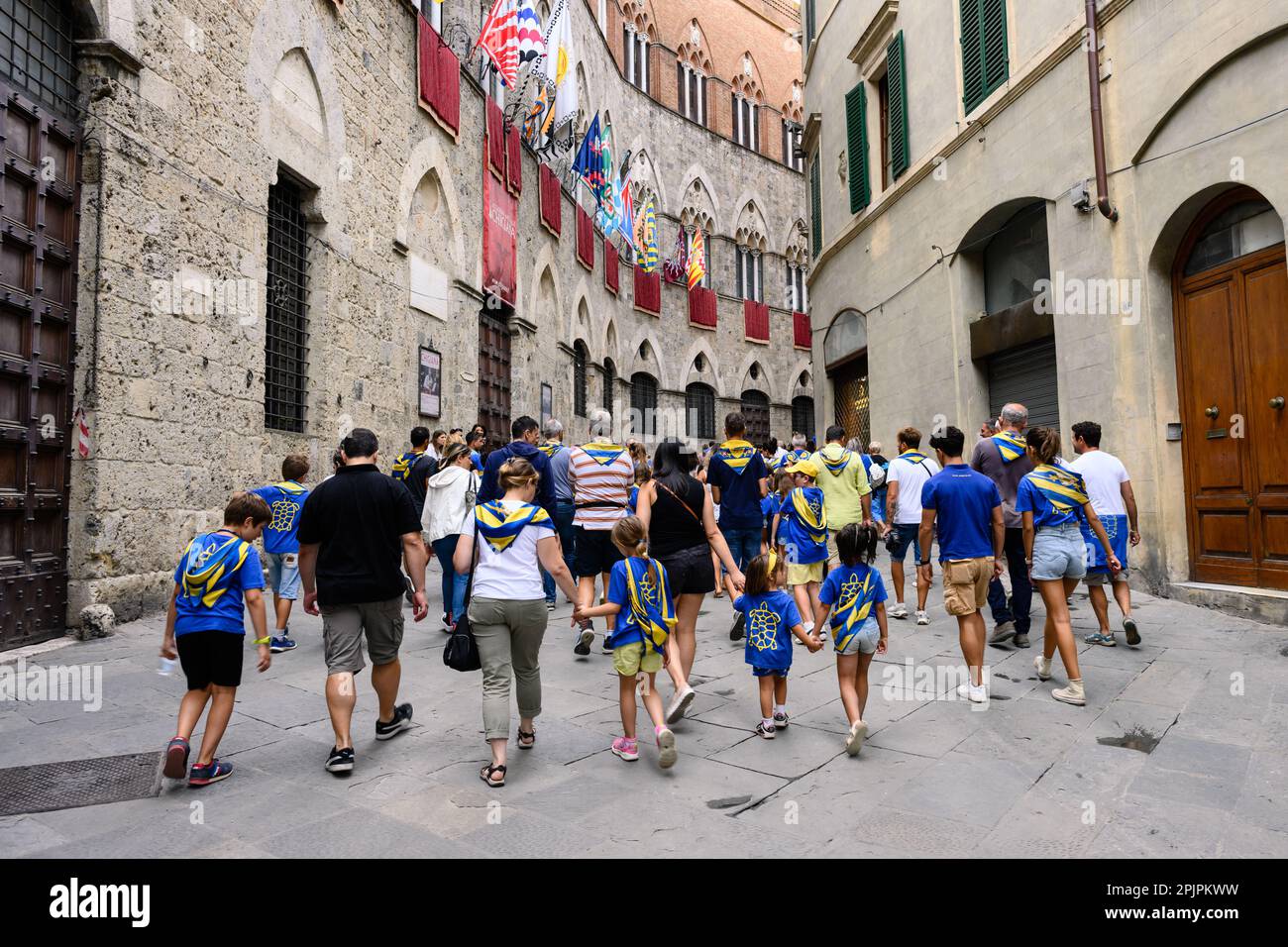 Siena, Italy - August 15 2022: Members of the Tartuca or Tortoise Contrada walking on Via di Citta in Front of the Palazzo Chigi-Saracini Stock Photo