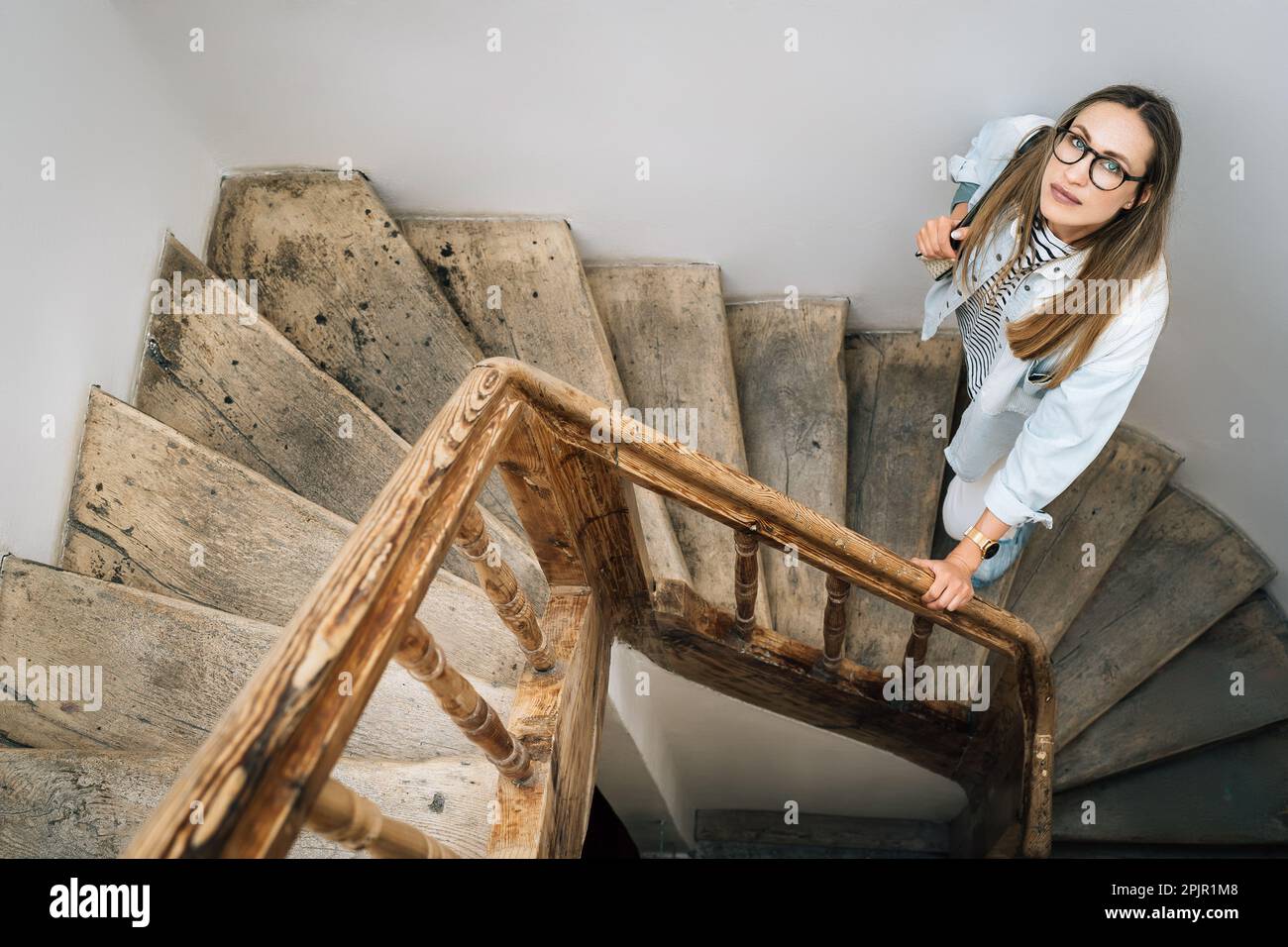 A woman looks up standing on an old wooden staircase Stock Photo