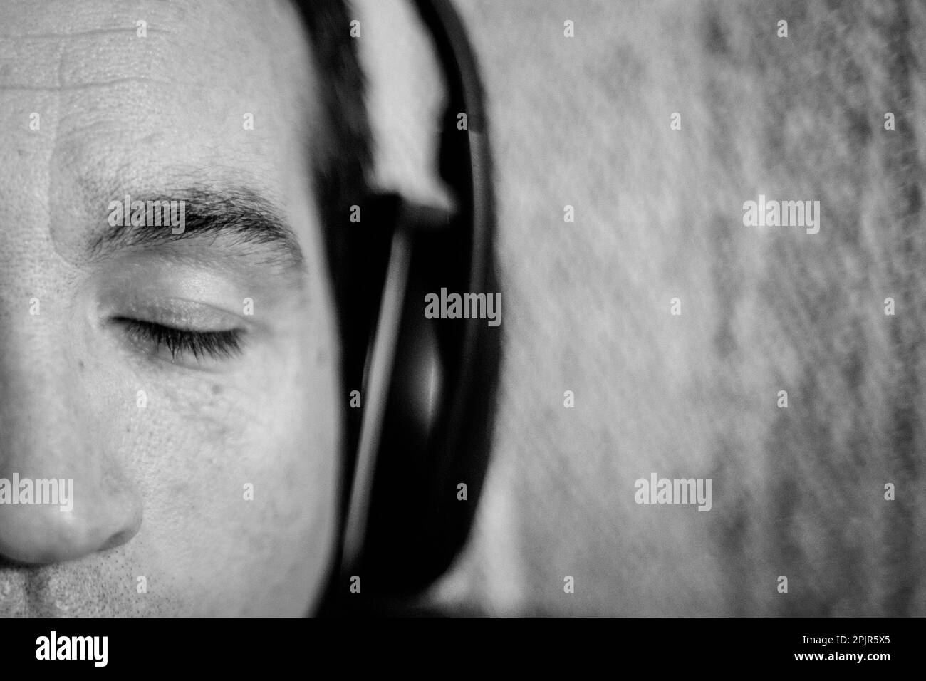 A close up of a man's face with his eyes closed.  The man is listening to music through headphones. Stock Photo
