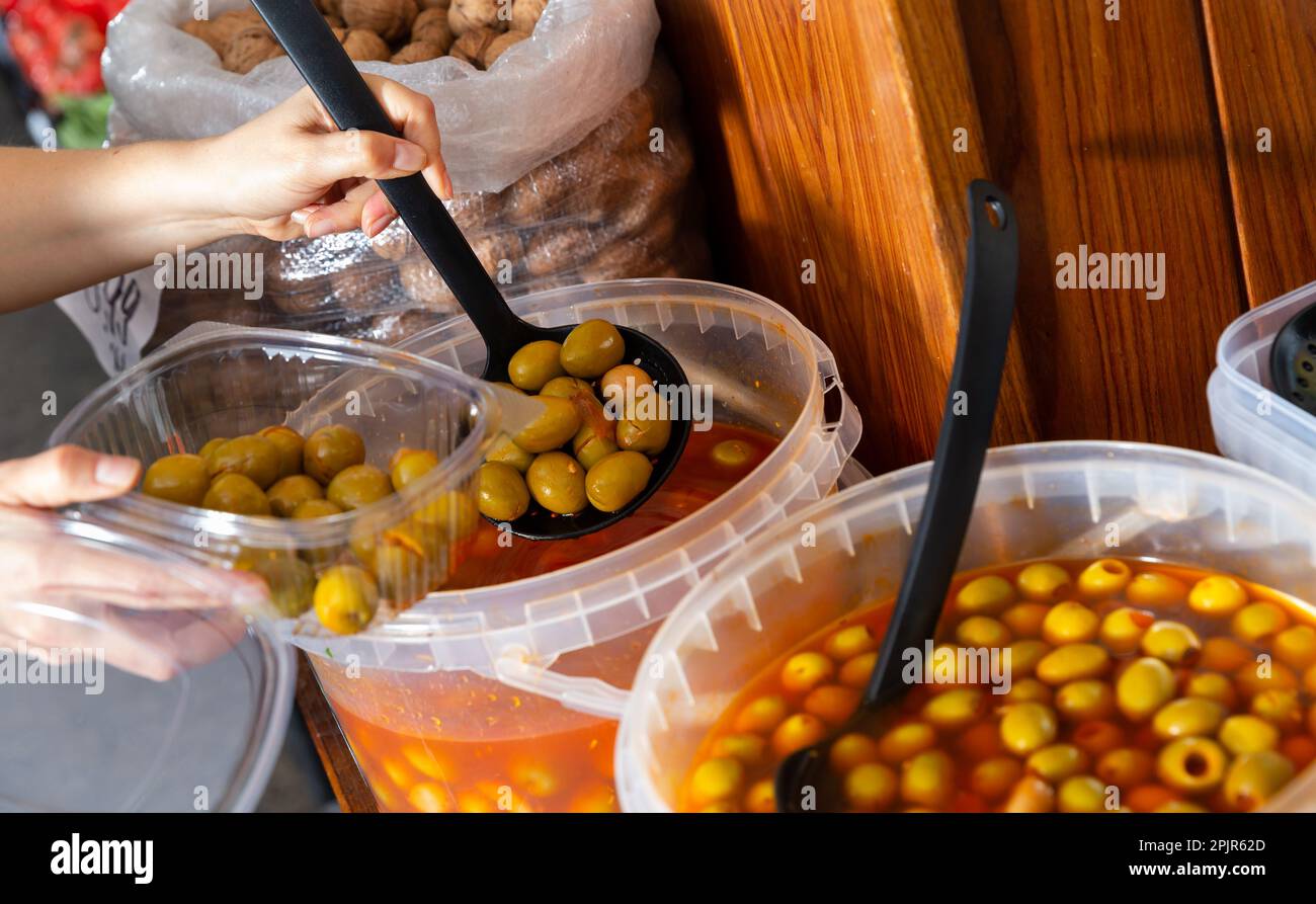 Female hands putting marinated olives from plastic bucket into container in store Stock Photo