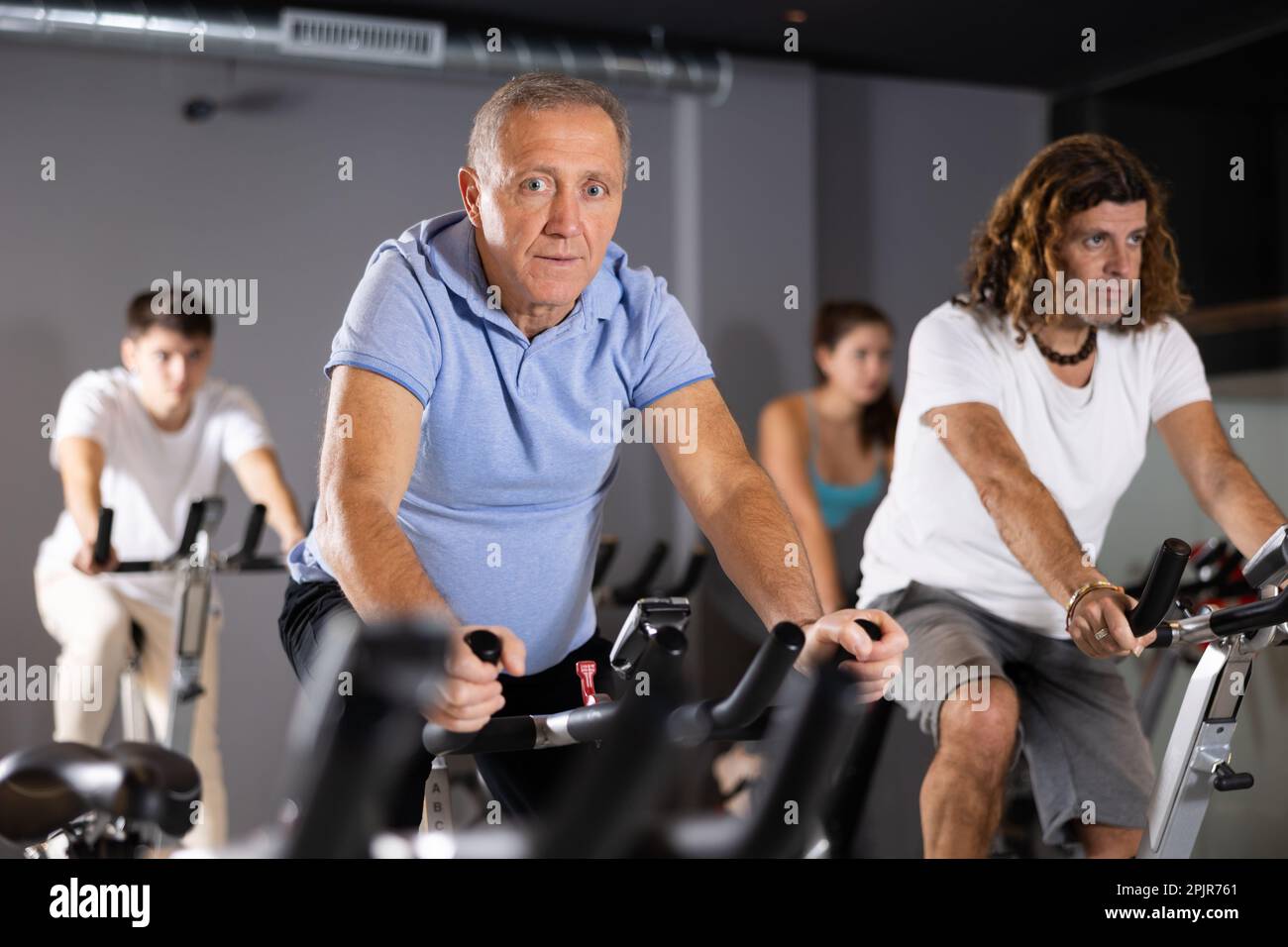Positive mature male riding exercise bike during cycling class in gym
