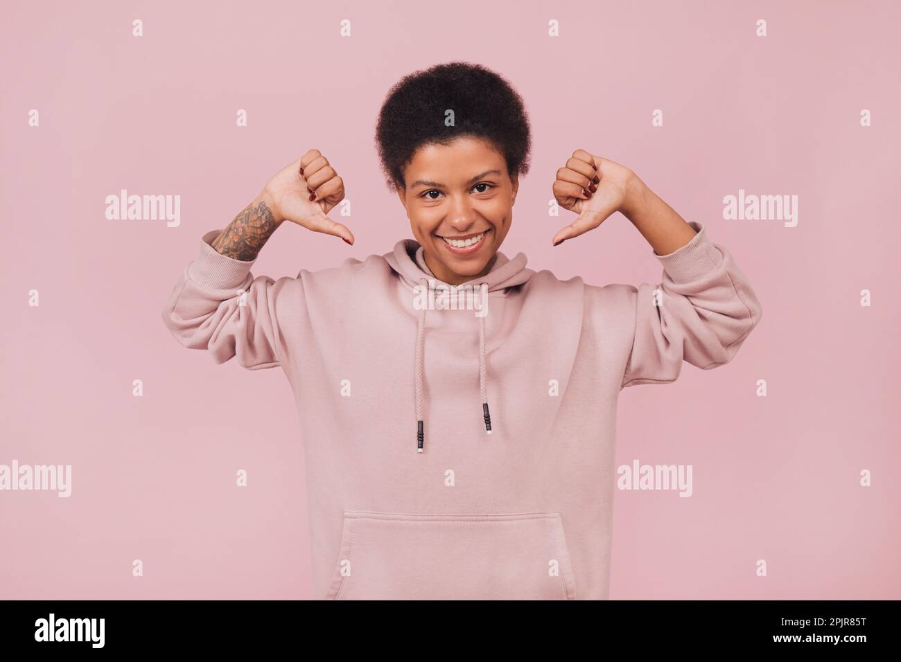 Joyful black girl raising her hands up and showing on herself. Cute smiling young woman wearing casual clothes posing on pink backdrop Stock Photo