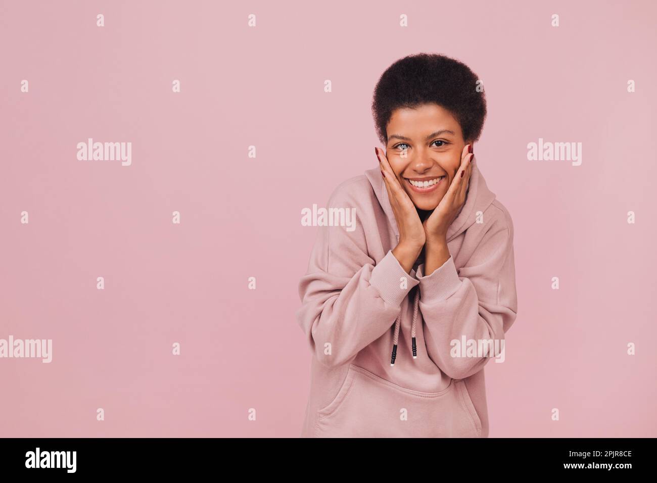 Surprised happy young black woman keeping her hands nears mouth. Pretty smiling girl wearing casual clothes posing over pink background Stock Photo