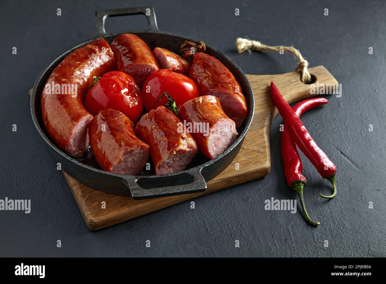 Fried pork sausage cut into pieces in a cast iron pan with tomatoes and