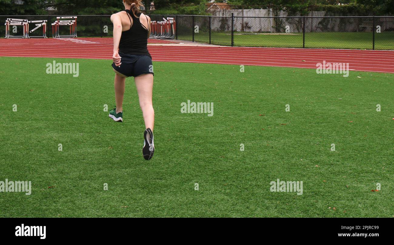 Rear view of a female runner in the air bounding on a green turf field