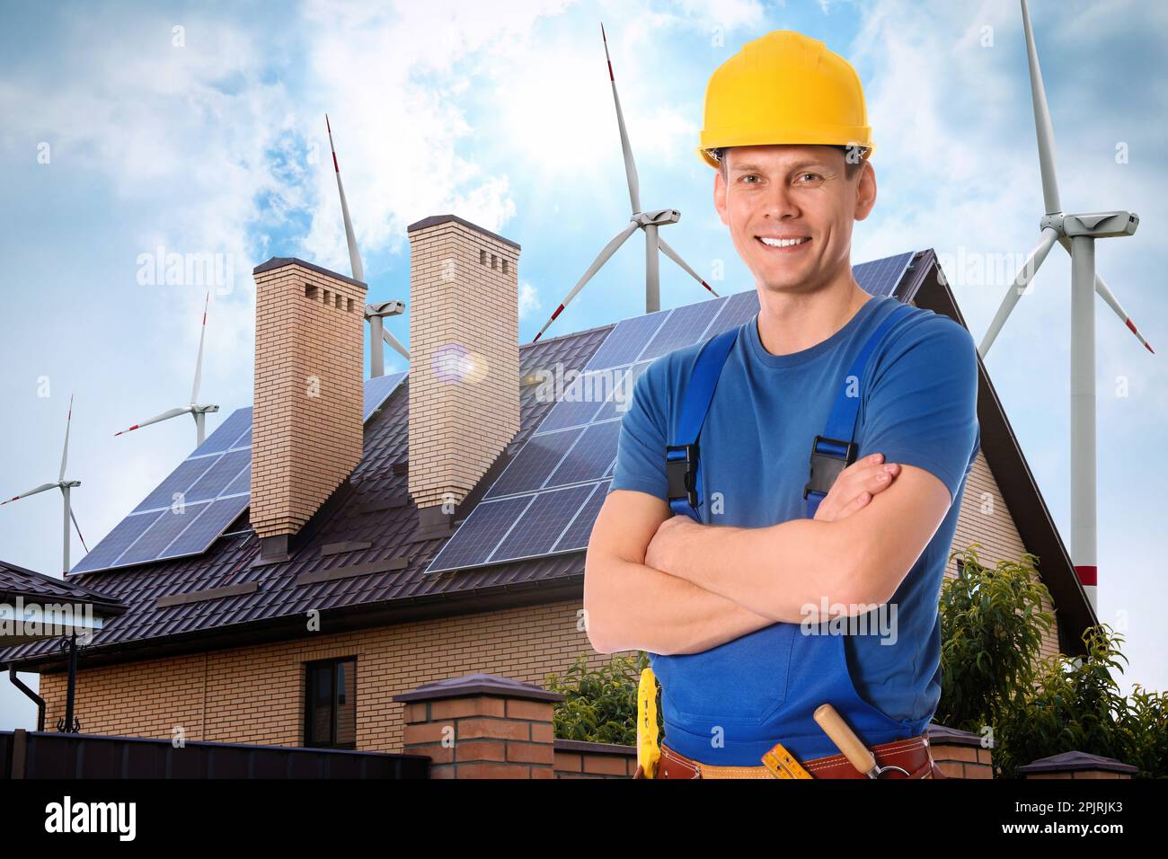 Worker with tool belt and view of wind energy turbines near house with