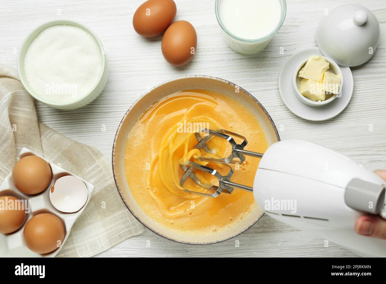 Woman beating eggs with mixer at white wooden table, top view Stock