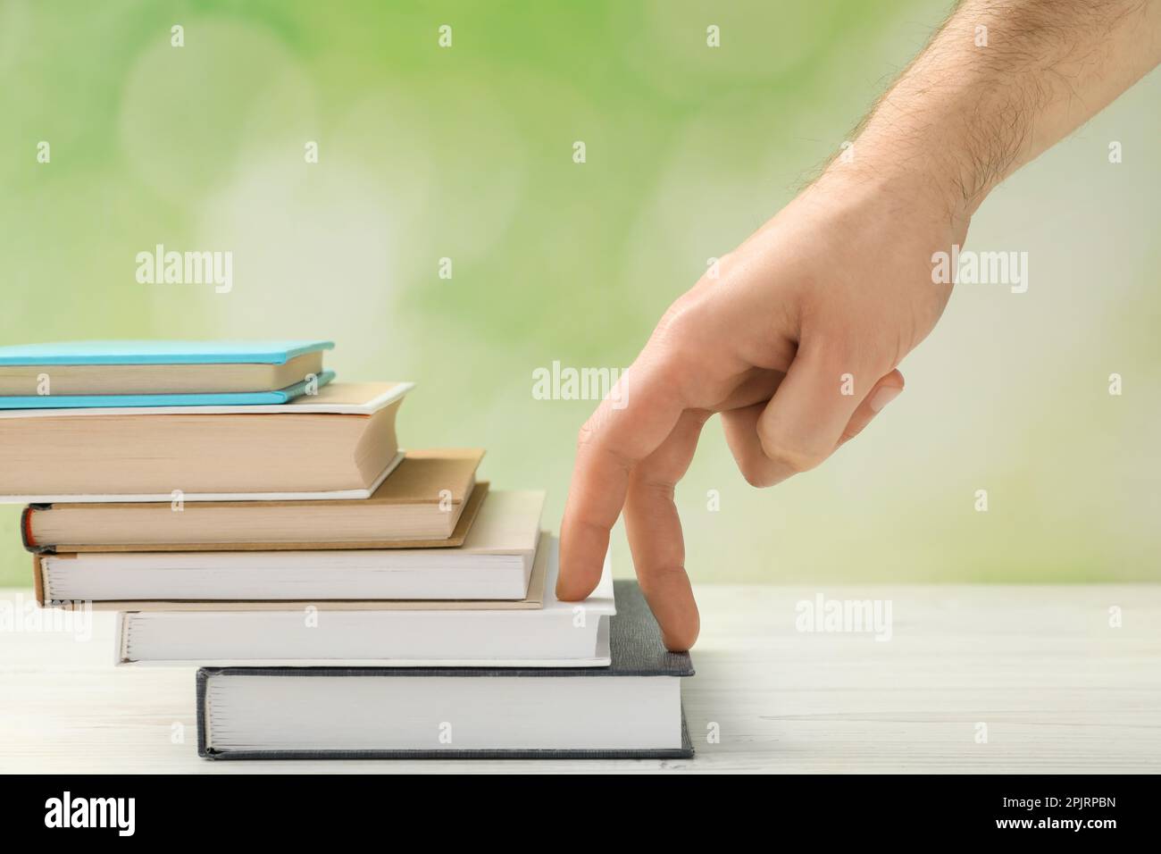 Man climbing up stairs of books with fingers on white wooden table against blurred background, closeup Stock Photo
