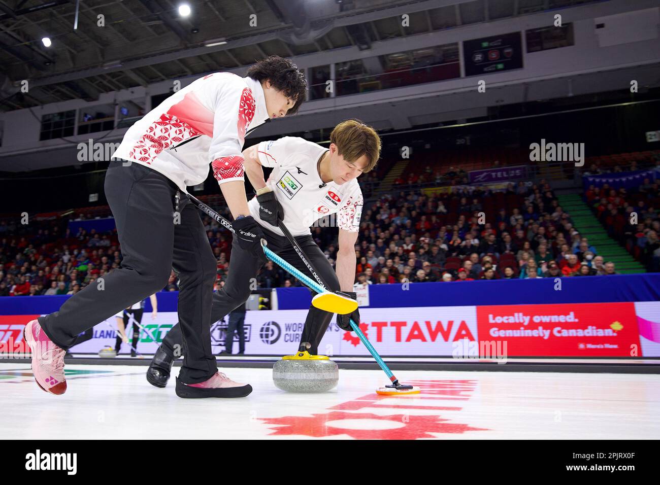 Takeru Yamamoto (L) and Satoshi Koizumi (R) sweep a stone during the 2023 World Mens Curling