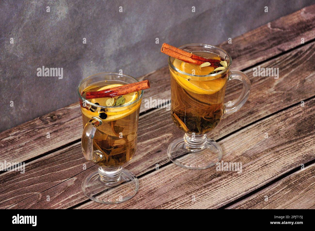 Two glasses with herbal tea, lemon slice and cinnamon sticks on a wooden table. Close-up. Stock Photo