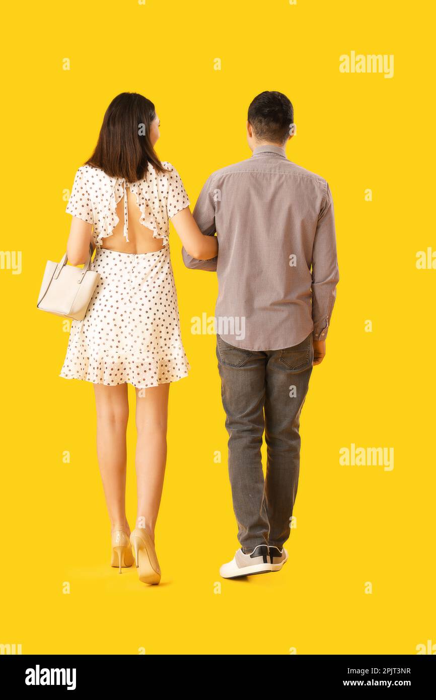 Lovely young couple walking hand in hand on yellow background, back ...