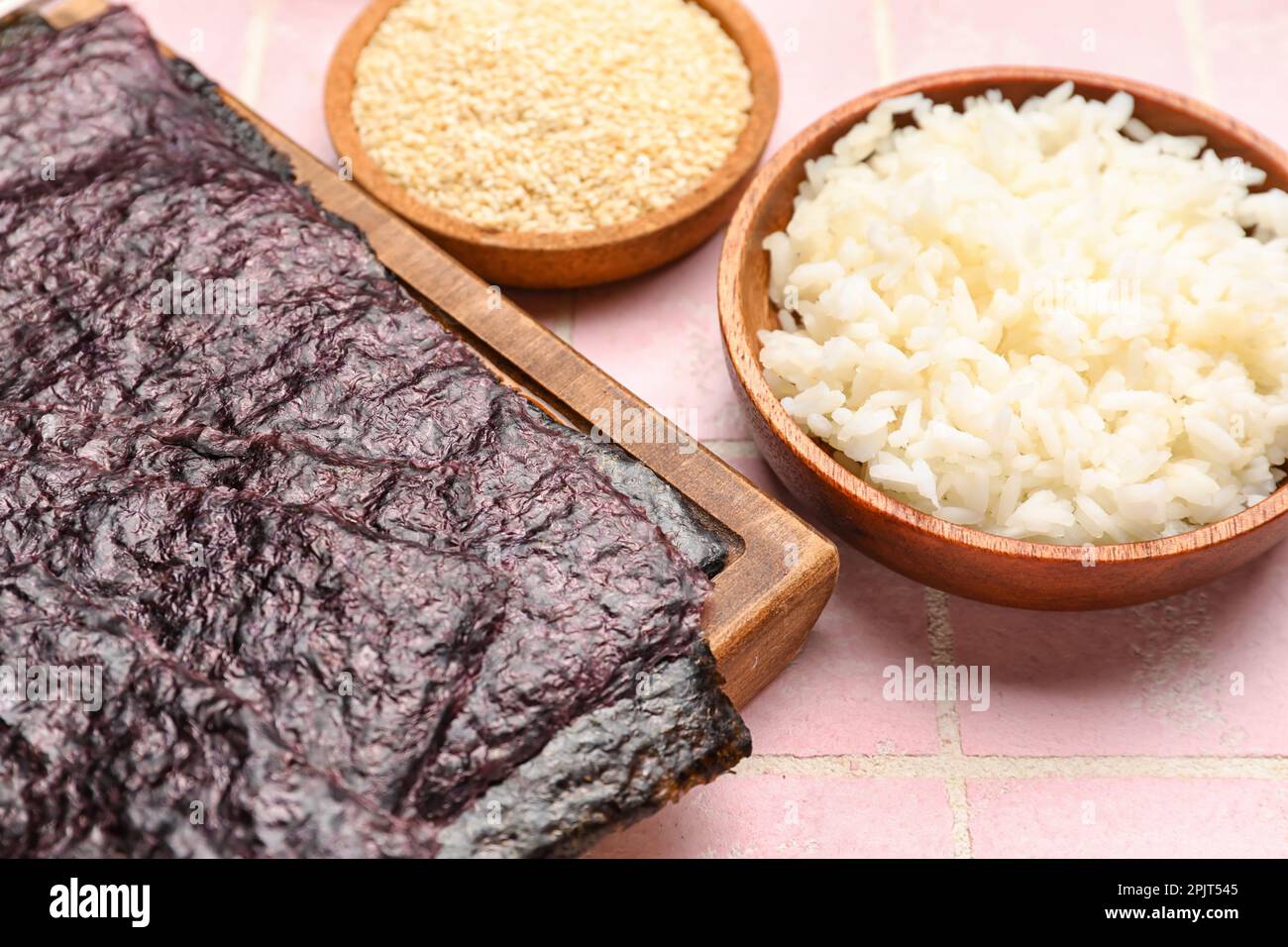 Noi Rice Wooden board with nori sheets and rice on pink tile background, closeup ...