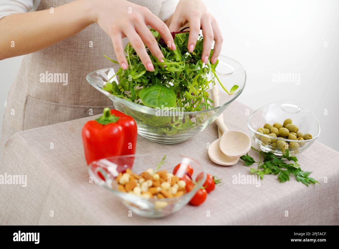 girl is stirs freshly prepared salad from arugula, cherry tomatoes, and mozzarella with your hands in a wooden bowl, around the ingredients are laid out top view. High quality photo Stock Photo