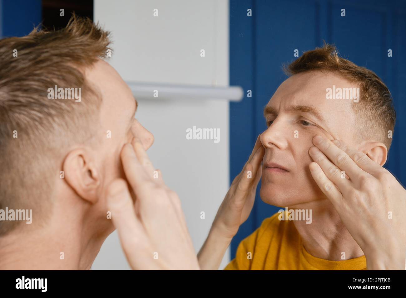 Concentrated man massaging and rubbing lotion under his eyes. Male aging problem. Stock Photo